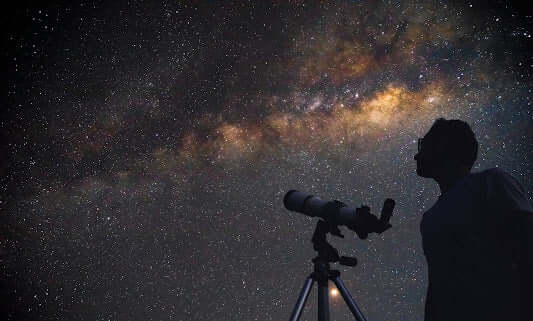Persona osserva le stelle con un telescopio sotto un cielo stellato, ideale per principianti che scelgono il primo telescopio.