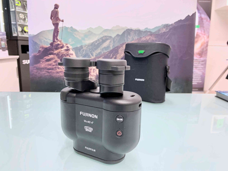 Binocolo Fujinon Techno-Stabi TS-X 14x40 su tavolo con immagine di montagna sullo sfondo, perfetto per applicazioni all'aperto.