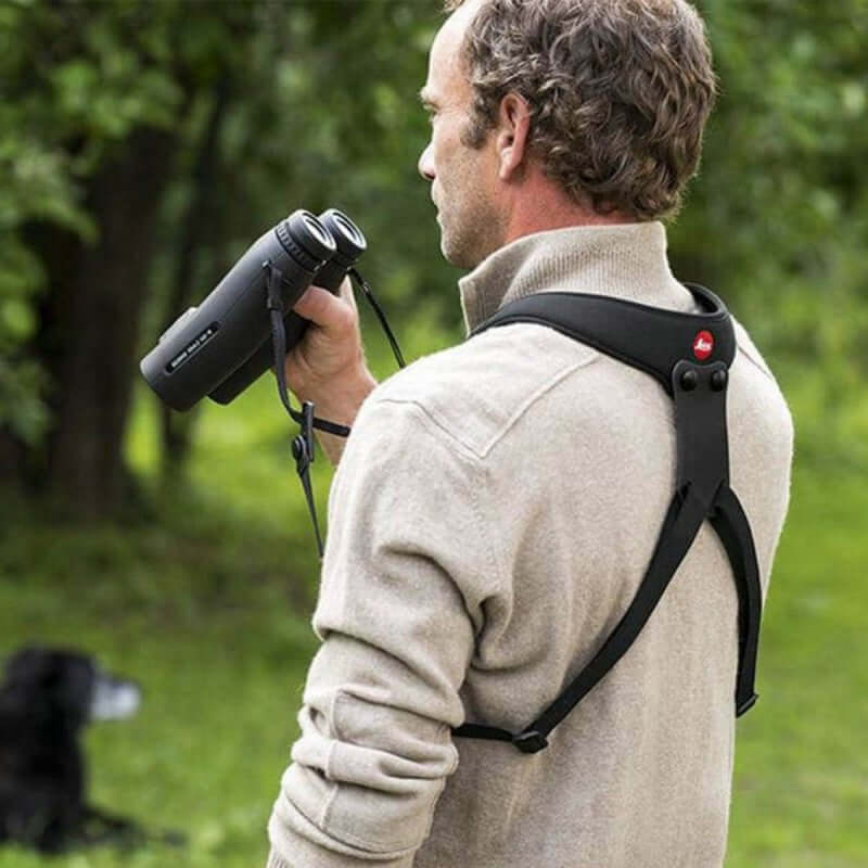 Uomo con binocolo indossa la Leica Bretella Sport in neoprene, ideale per camminata e arrampicata con accesso rapido al binocolo.