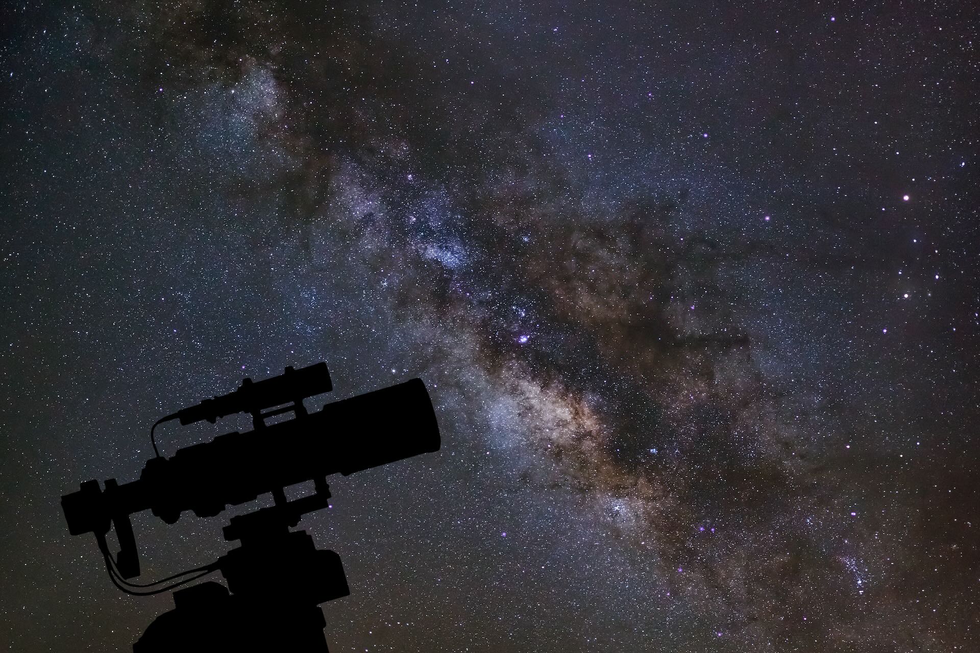 Silhouette of a telescope against the starry night sky and Milky Way galaxy